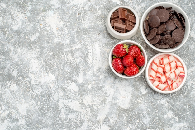 Vista dall'alto ciotole con fragole, caramelle e cioccolatini in alto a destra del fondo bianco-grigio