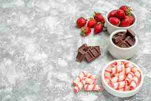 Бесплатное фото Вид сверху чаши с клубникой, шоколадными конфетами и некоторыми клубничными шоколадными конфетами с правой стороны серо-белого мозаичного стола