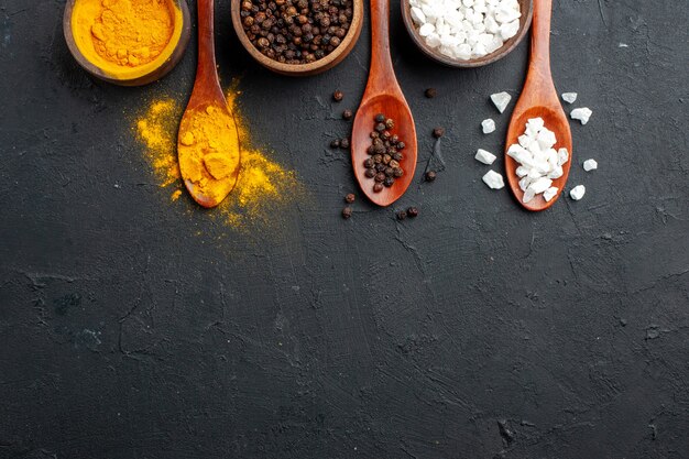 Free photo top view bowls with turmeric black pepper sae salt wooden spoons on black surface copy place