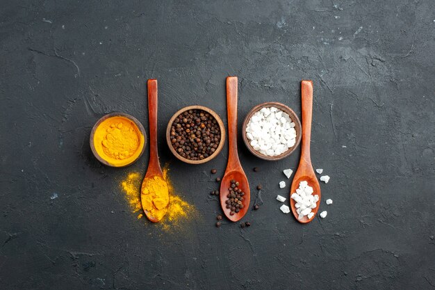 Top view bowls with turmeric black pepper sae salt wooden spoons on black surface with copy place