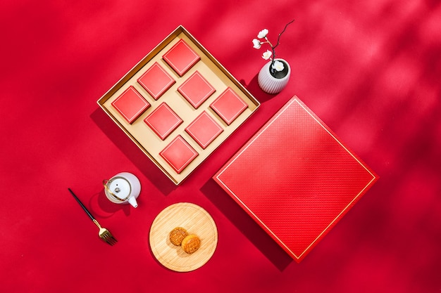 Top view of a box of mooncakes with teapot, fork, and vase on a red surface