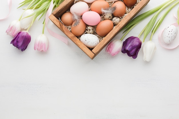 Foto gratuita vista dall'alto della scatola con uova per pasqua e tulipani colorati