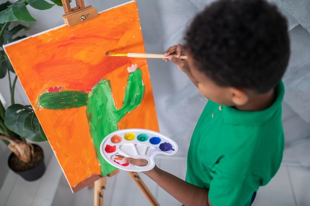 Top view of boy with palette painting on easel