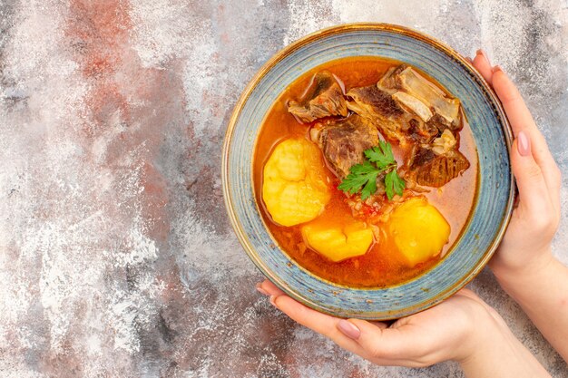 Top view bozbash soup in a bowl in female hand on nude background