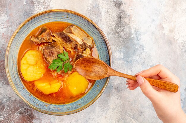 Top view bozbash soup in a bowl a wooden spoonn in female hand on nude background