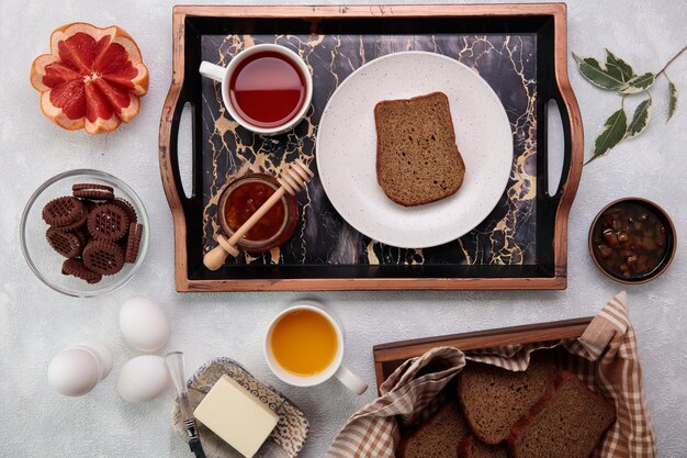 Top view of bread slice quince jam cup of tea in tray with cookies grapefruit cup of orange juice eggs and butter on white background