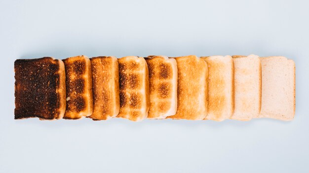 Top view of bread slices at varying stages of toasting arranged in row on white background