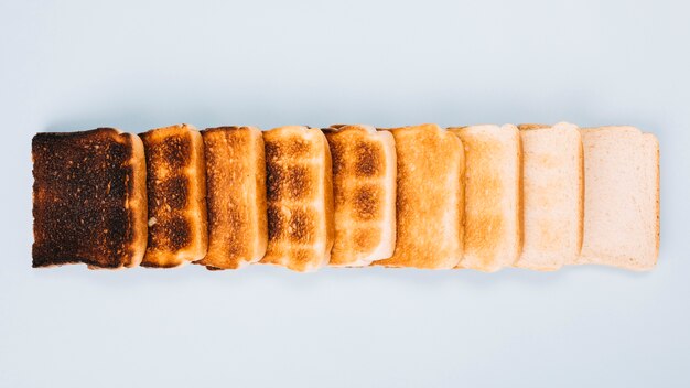 Вид сверху кусочки хлеба на различных этапах тостов, расположенных в ряд на белом фоне