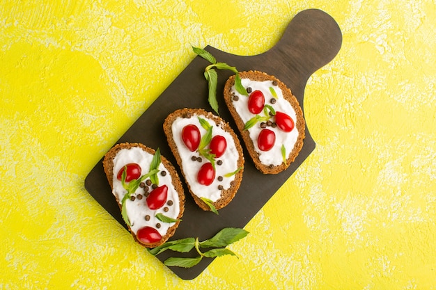 Vista dall'alto di toast di pane con panna acida e cornioli sulla scrivania gialla