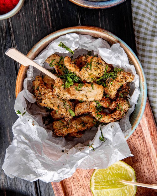 Top view of breaded chicken with herbs in a bowl on wood