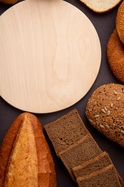 Top view of breads as baguette cob rye bread slices with cutting board on maroon background