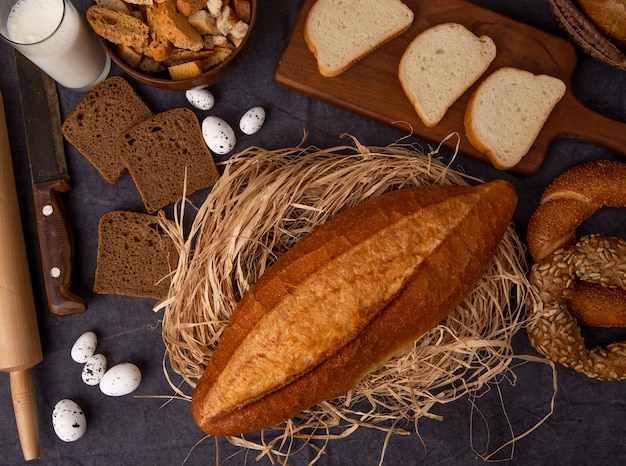 Вид сверху хлеба в виде багета на соломенной ржи и бублика из белого хлеба с молочными яйцами на бордовом фоне