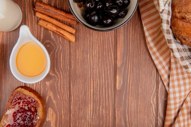 Vista dall'alto di pane come pane nero fetta di pane di segale spalmato di marmellata burro cannella olive nel latte ciotola su fondo in legno con spazio di copia