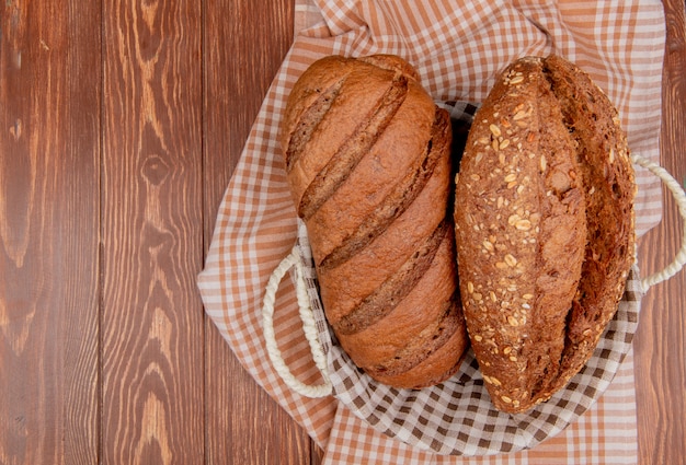 top view of breads as black and seeded baguette in basket on plaid cloth and wooden table with copy space