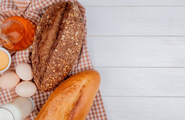 Top view of breads as black seeded and vietnamese baguette with eggs butter milk on plaid cloth and wooden background with copy space