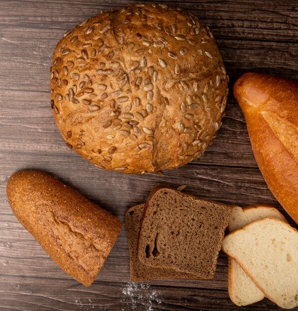 Top view of breads as brown seeded cob baguette rye and white ones on wooden background