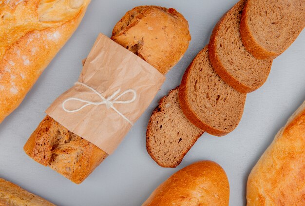 Top view of breads as crispy black and white baguettes with sliced rye bread on blue table