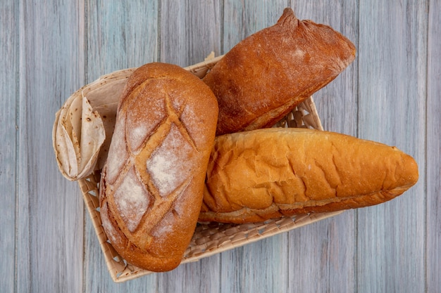 Top view of breads as crusty flatbread and baguette in basket on wooden background