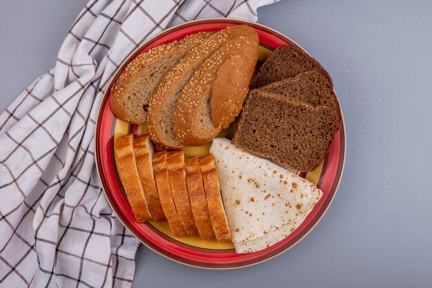 회색 배경에 격자 무늬 천으로 접시에 썰어 시드 갈색 옥수수 속 호밀 바게트와 플랫 브레드로 빵의 상위 뷰