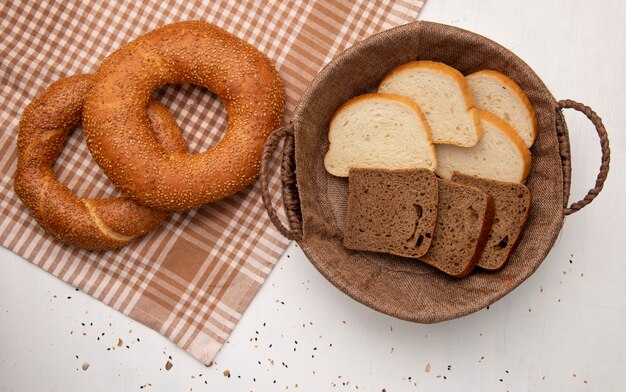 Top view of breads as turkish bagel on cloth and basket with white and rye bread slices on white background