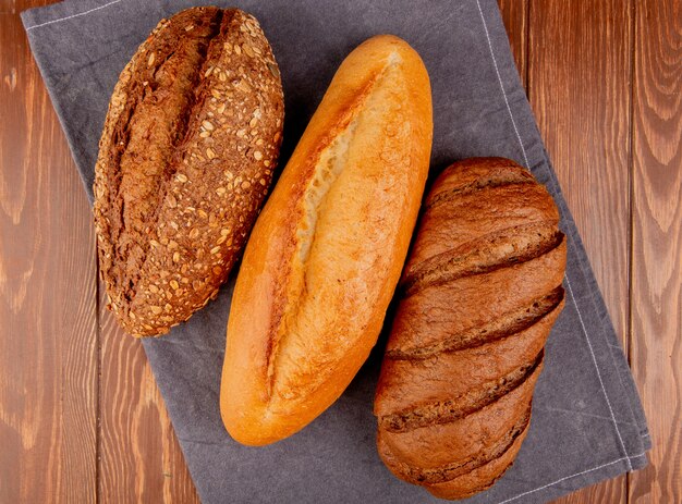 top view of breads as vietnamese and black seeded baguette and black bread on gray cloth and wooden table