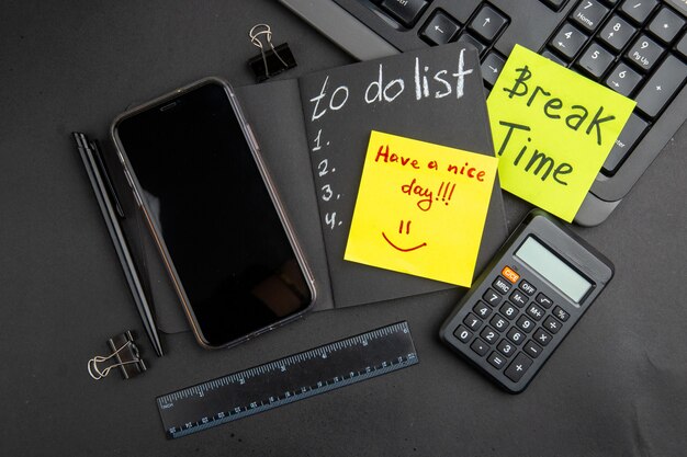 Top view break time and have a nice day written on sticky notes to do list on black notepad phone pen calculator ruler binder clips keyboard on black table