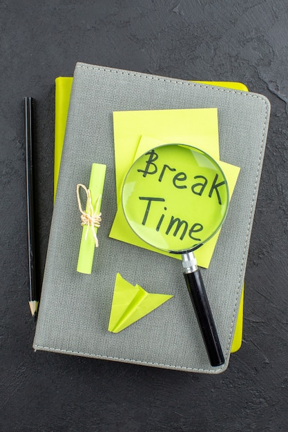 Top view break time written on yellow sticky notes lupa black pencil on notepads on dark table