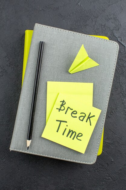 Top view break time written on yellow sticky notes paper plane black pencil on notepads on dark table