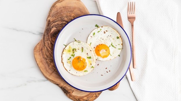 Top view of breakfast fried eggs on plate with cutlery