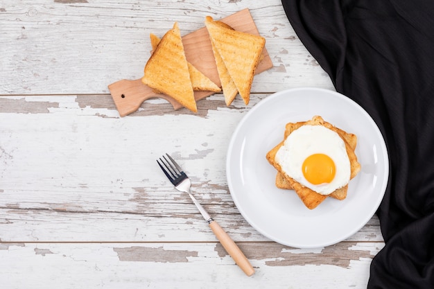 Top view of breakfast fried eggs on white plate with toast and copy space on wooden surface horizontal