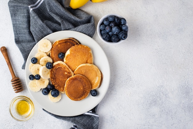 Top view of breakfast pancakes on plate with honey and blueberries