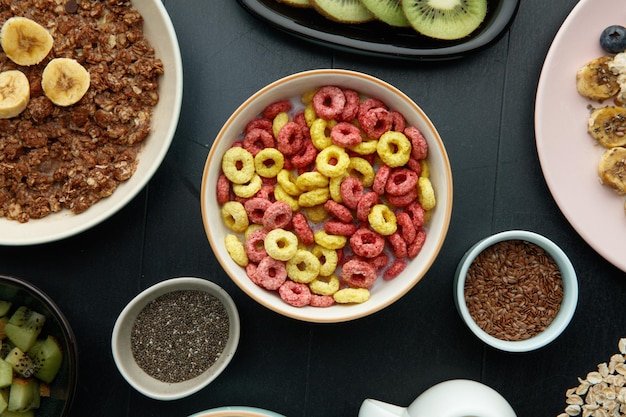 Vista dall'alto del set per la colazione con ciotole di farina d'avena di cereali e banana e noci con fette di kiwi chia e semi di lino su sfondo nero