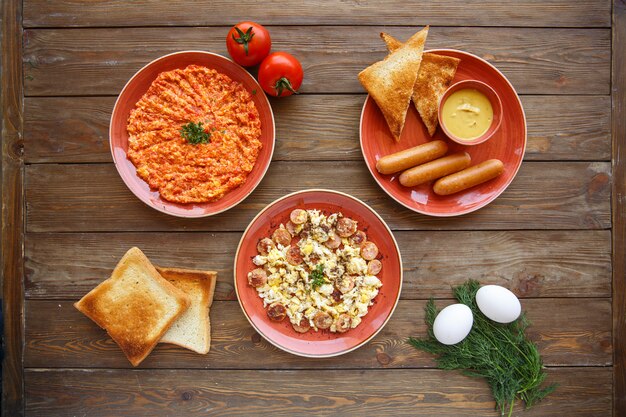 Top view of breakfast setup with egg and tomato dish and sausages dishes