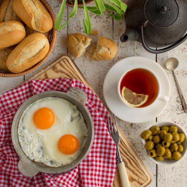 Top view of breakfast setup with eggs, olives, bread and black tea