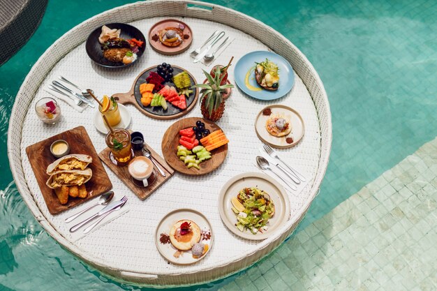 Top view on  Breakfast tray in swimming pool, floating breakfast in luxury hotel smoothies and fruit plate. Exotic summer diet. Tropical beach lifestyle. Bali style.