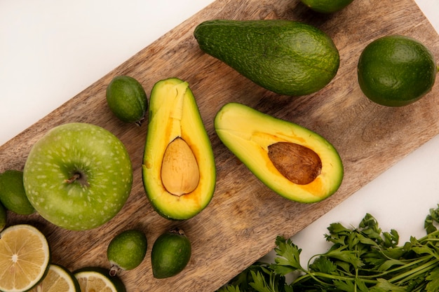 Top view of bright green avocados on a wooden kitchen board with apples limes and feijoas on a white surface