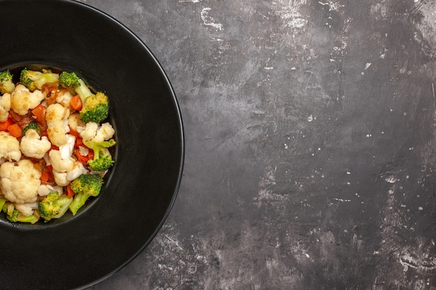 上面図ブロッコリーとカリフラワーのサラダ、暗い背景の黒い楕円形のプレート、コピースペースの食べ物の写真