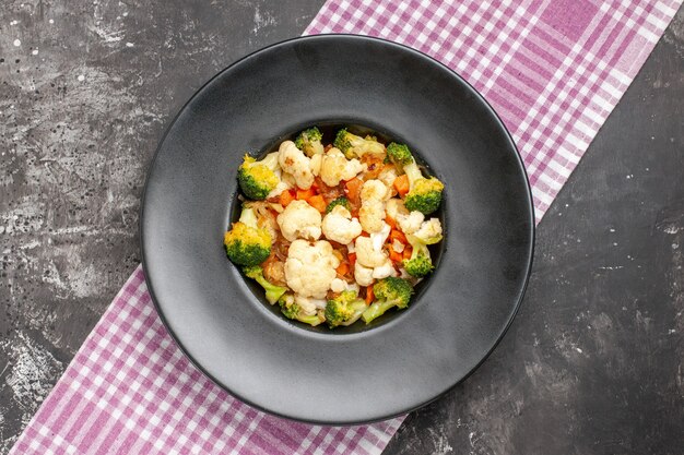 Top view broccoli and cauliflower salad on black oval plate pink and white checkered tablecloth on dark surface free space