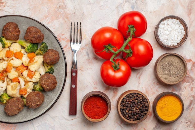 누드 배경에 다채로운 향신료와 포크 토마토와 함께 접시 그릇에 상위 뷰 브로콜리와 콜리플라워 샐러드와 미트볼