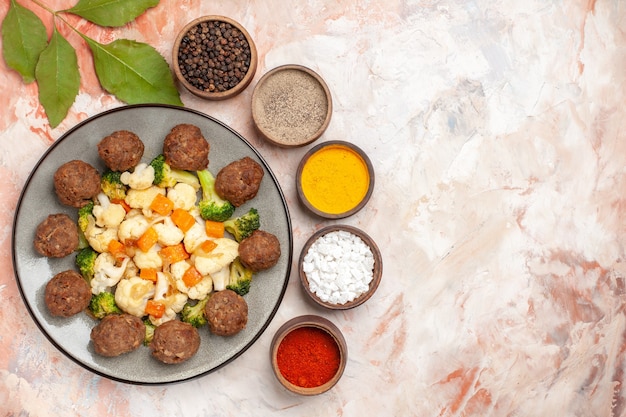 Free photo top view broccoli and cauliflower salad and meatball on plate different spices in small bowls leaves on nude isolated background with free place