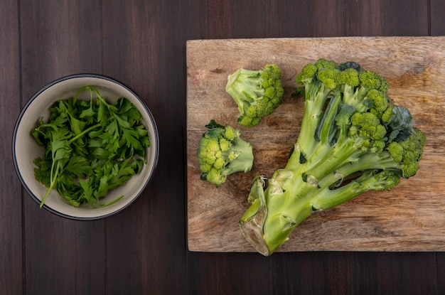Top view broccoli on cutting board with parsley in bowl on wooden background