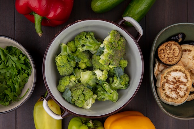 Top view broccoli in a saucepan with parsley in a bowl with and cucumbers on wooden background