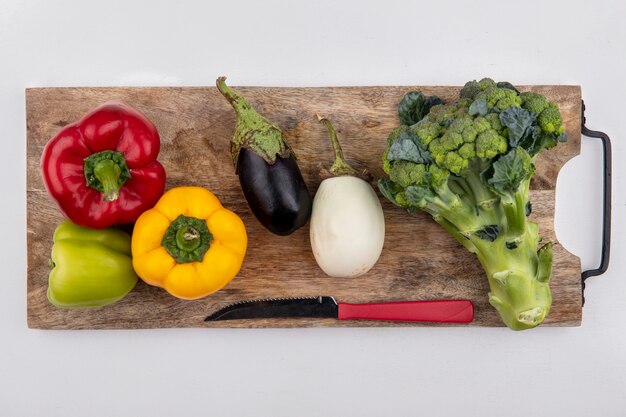 Top view broccoli with black and   white eggplant with colored bell peppers and a knife on a cutting board