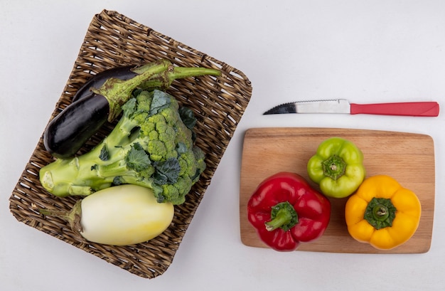 Vista dall'alto broccoli con melanzane bianche e nere su un supporto con peperone colorato su un tagliere e un coltello su sfondo bianco