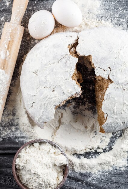 Top view broken cake with rolling pin, flour, eggs on dark wooden surface. vertical