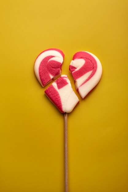 Top view broken heart shaped candy on yellow background