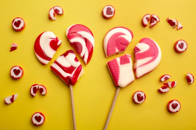 Top view broken hearts lollipops on yellow background