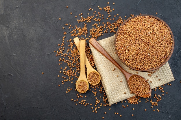 top view brown buckwheat inside plate with pair of spoons on dark background