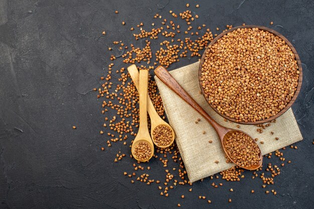 top view brown buckwheat inside plate with pair of spoons on dark background