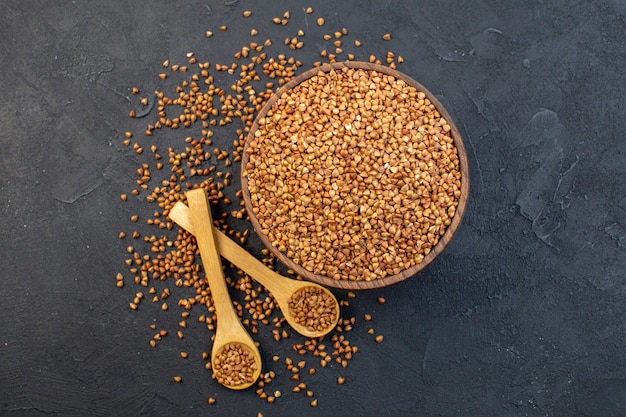 top view brown buckwheat inside plate with pair of spoons on dark background